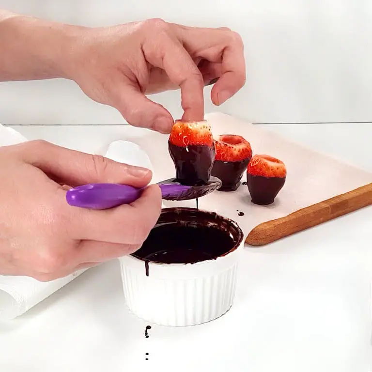 Dipping strawberry in melted chocolate.
