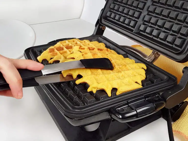 Lifting cooked waffle from the iron with tongs.