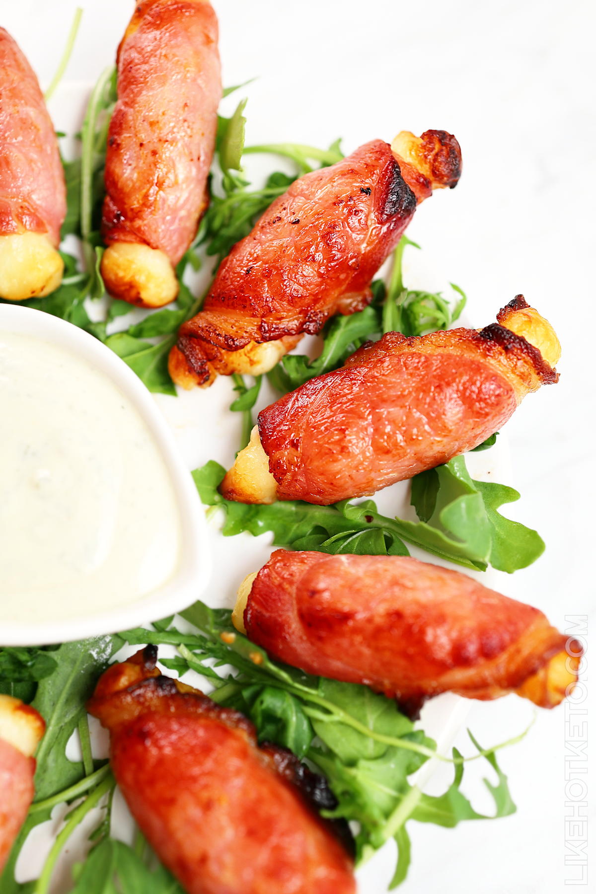 A plate of crispy air fried bacon wrapped halloumi cheese on a bed of arugula leaves.