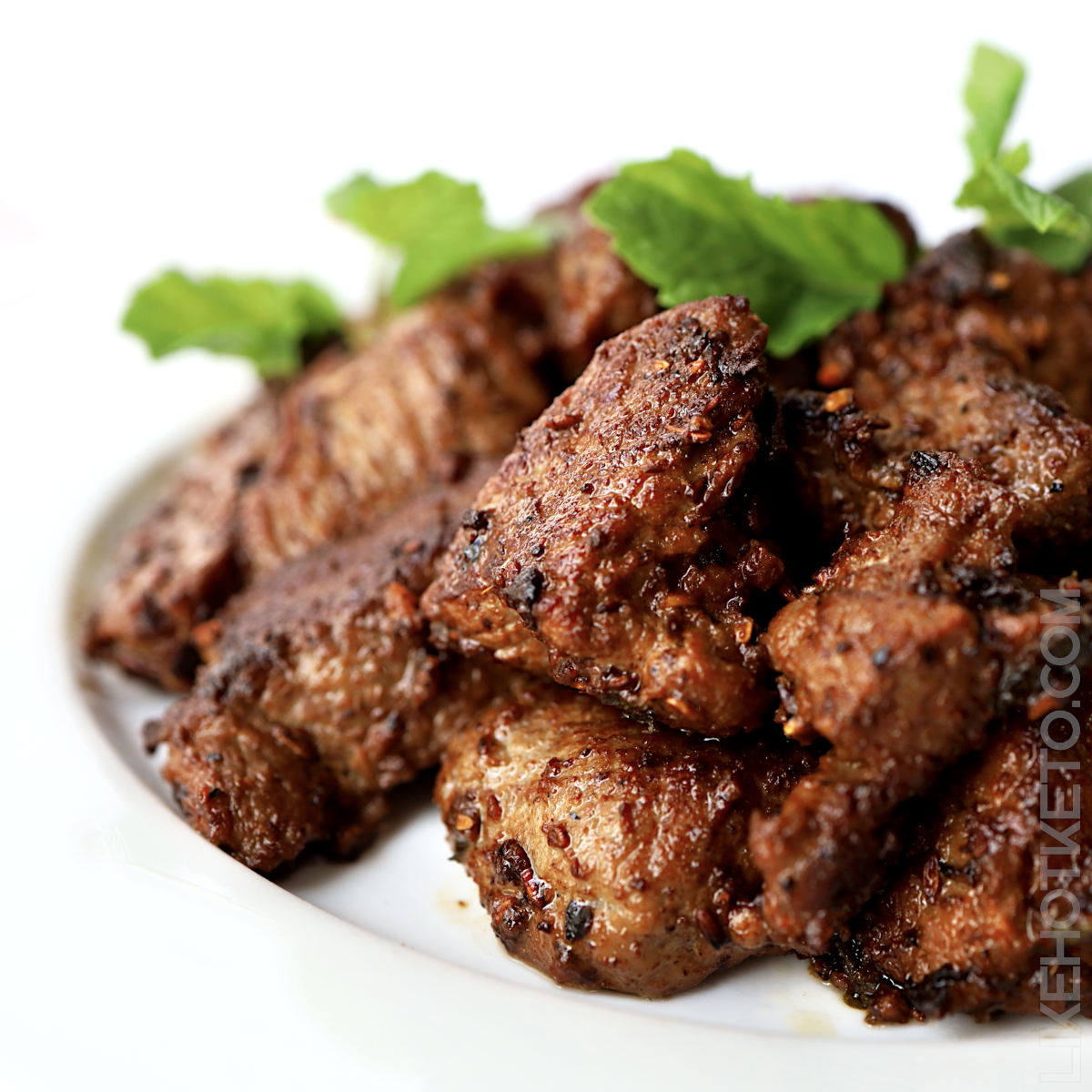 A plate with cooked camel meat pieces in yogurt garnished with fresh mint leaves.