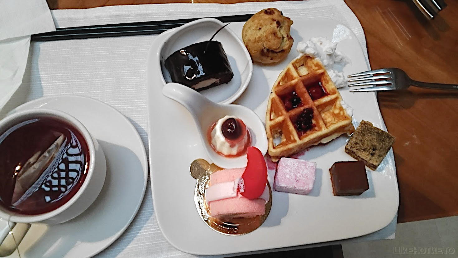 Plate with an assortment of fancy sweets, with a small panna cotta in the center, next to a cup of tea.