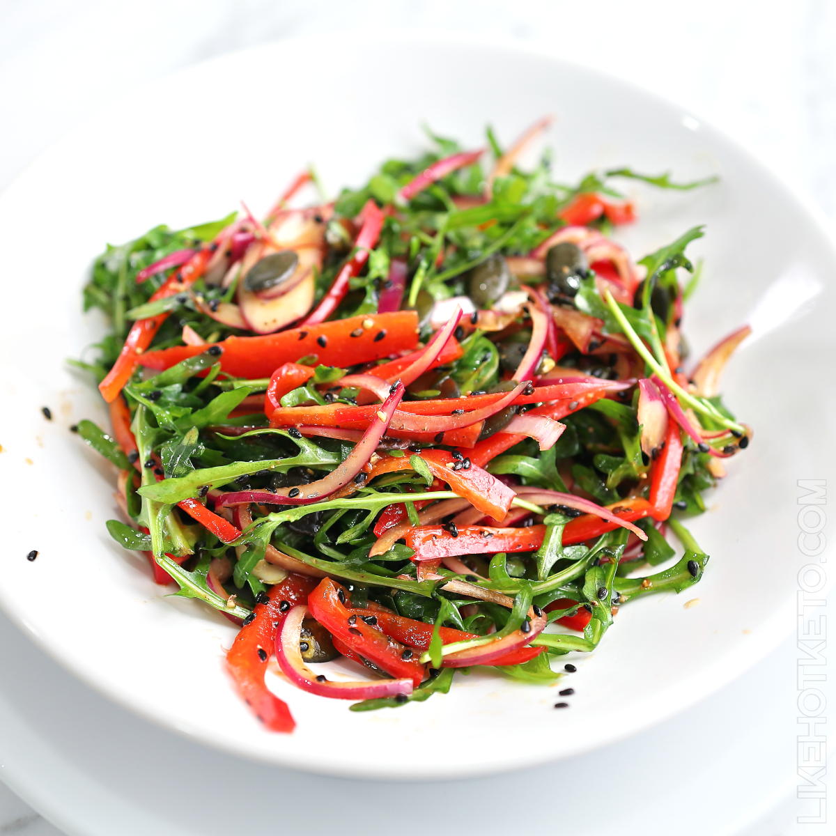 Colorful salad with arugula, red peppers and red onions, sprinkled with black sesame.