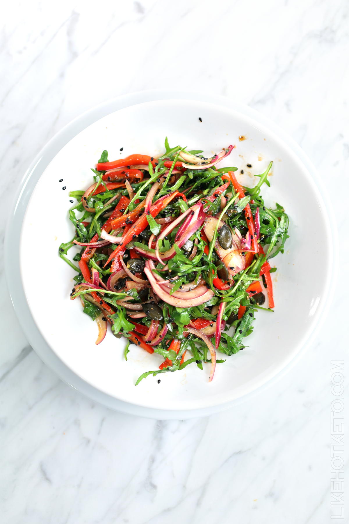 Colorful arugula salad with pepitas and black sesame, red onion and pepper.
