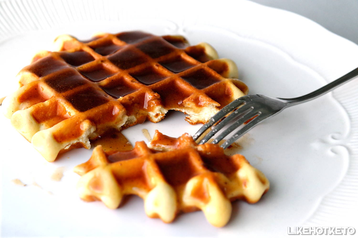 A keto waffle topped with sugar-free maple syrup, cut with a fork, syrup drizzling away over the plate.