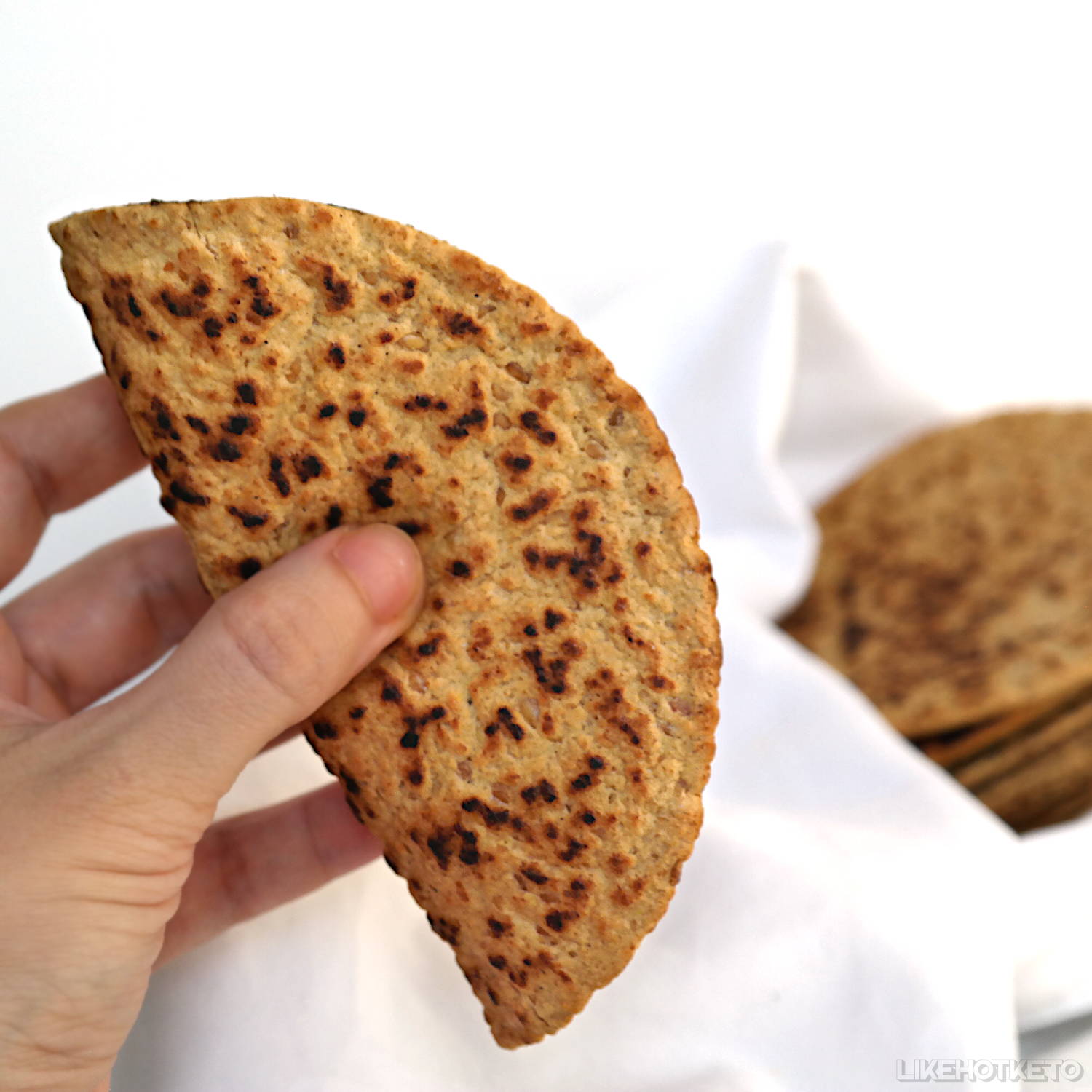 A keto flax meal and pea protein tortilla wrap, folded in between fingers to show  its flexible, soft texture.