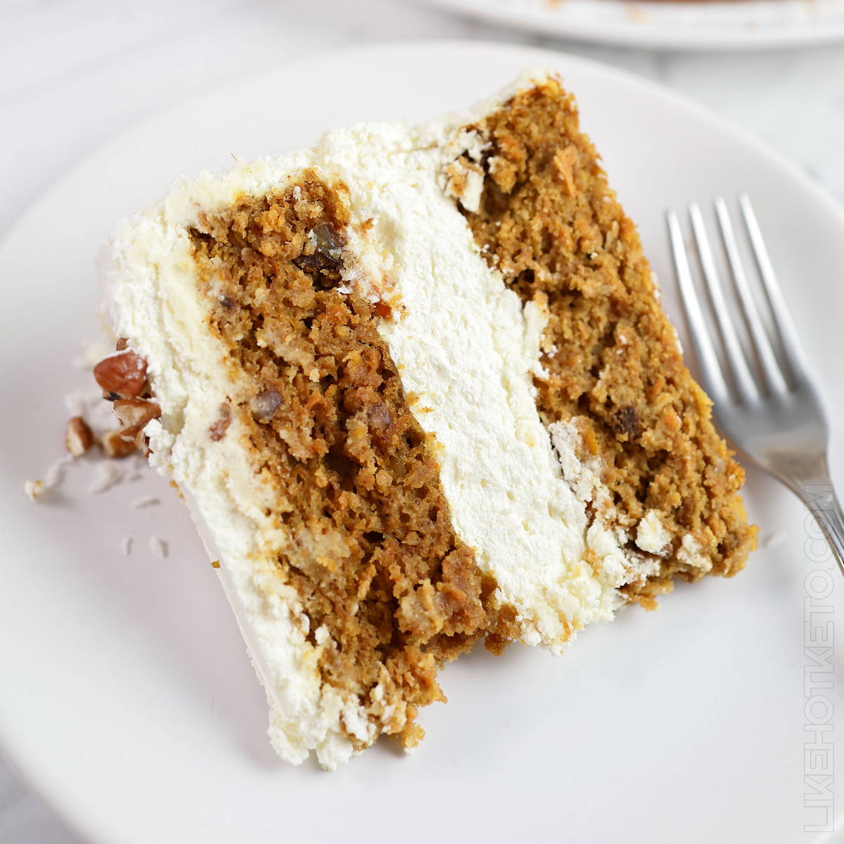 A slice of carrot cake with a thick cream cheese sugar-free frosting filling, on a white plate.