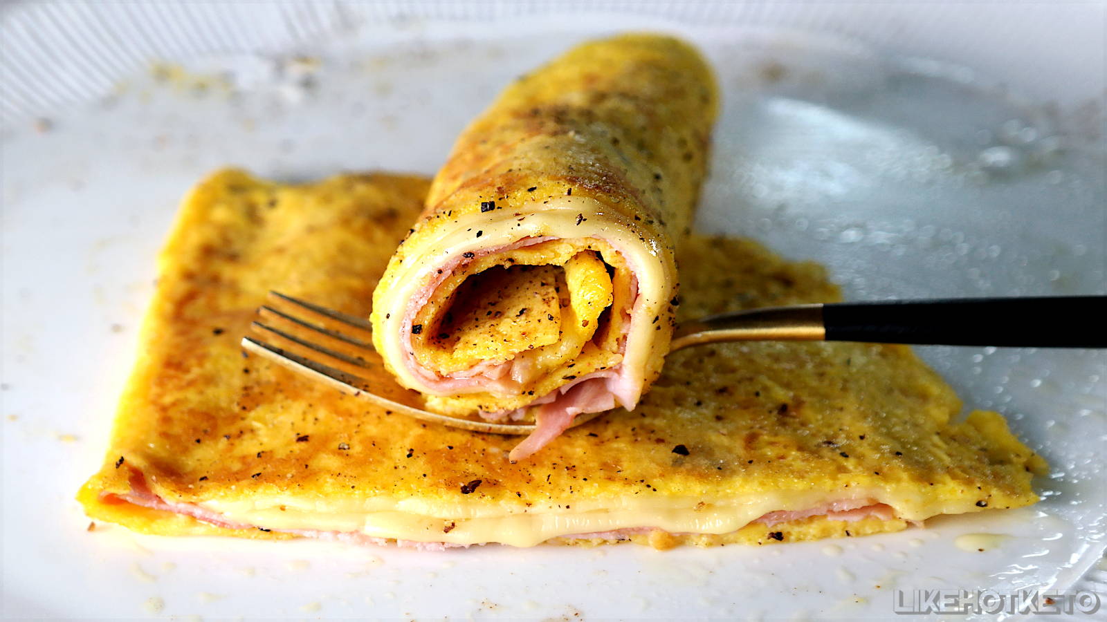 Half of a keto egg crêpe rolled over a golden fork, with the melted cheese filling oozing out.