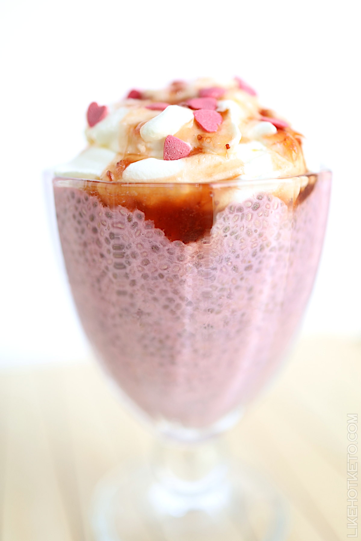 Strawberry pink keto chia pudding with whipped cream and heart sprinkles.