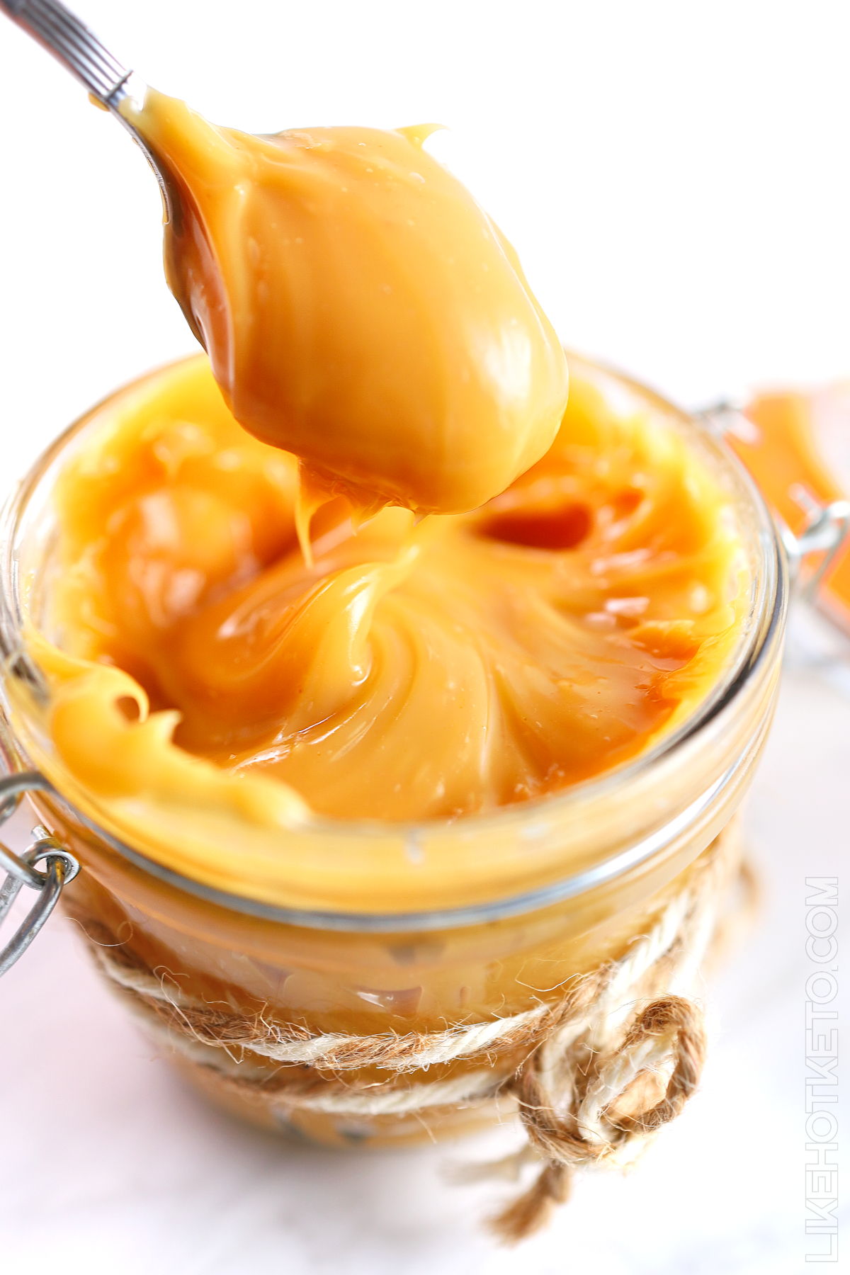 A spoonful of keto dulce de leche caramel, lifted from mason jar tied up with decorative cord.