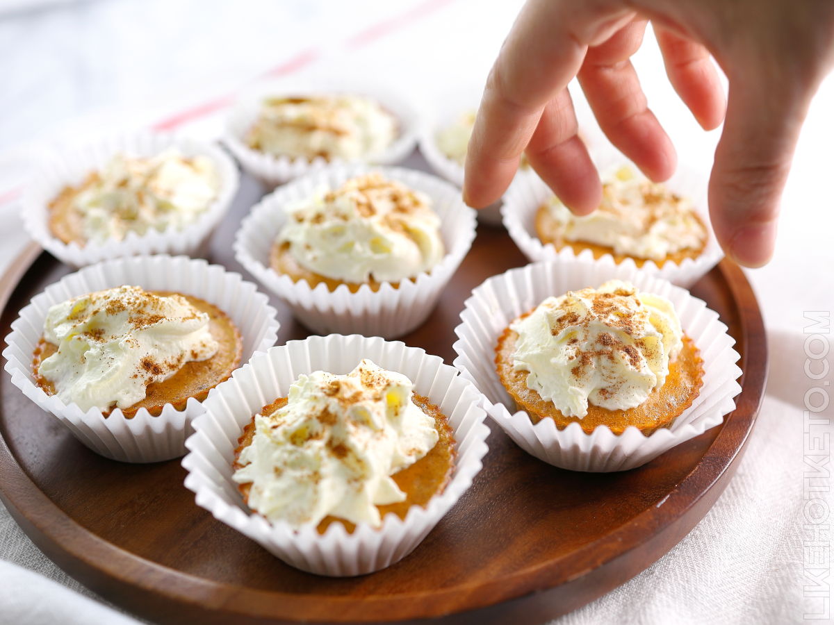 A hand grabbing from a plate full of keto mini pumpkin protein pies.
