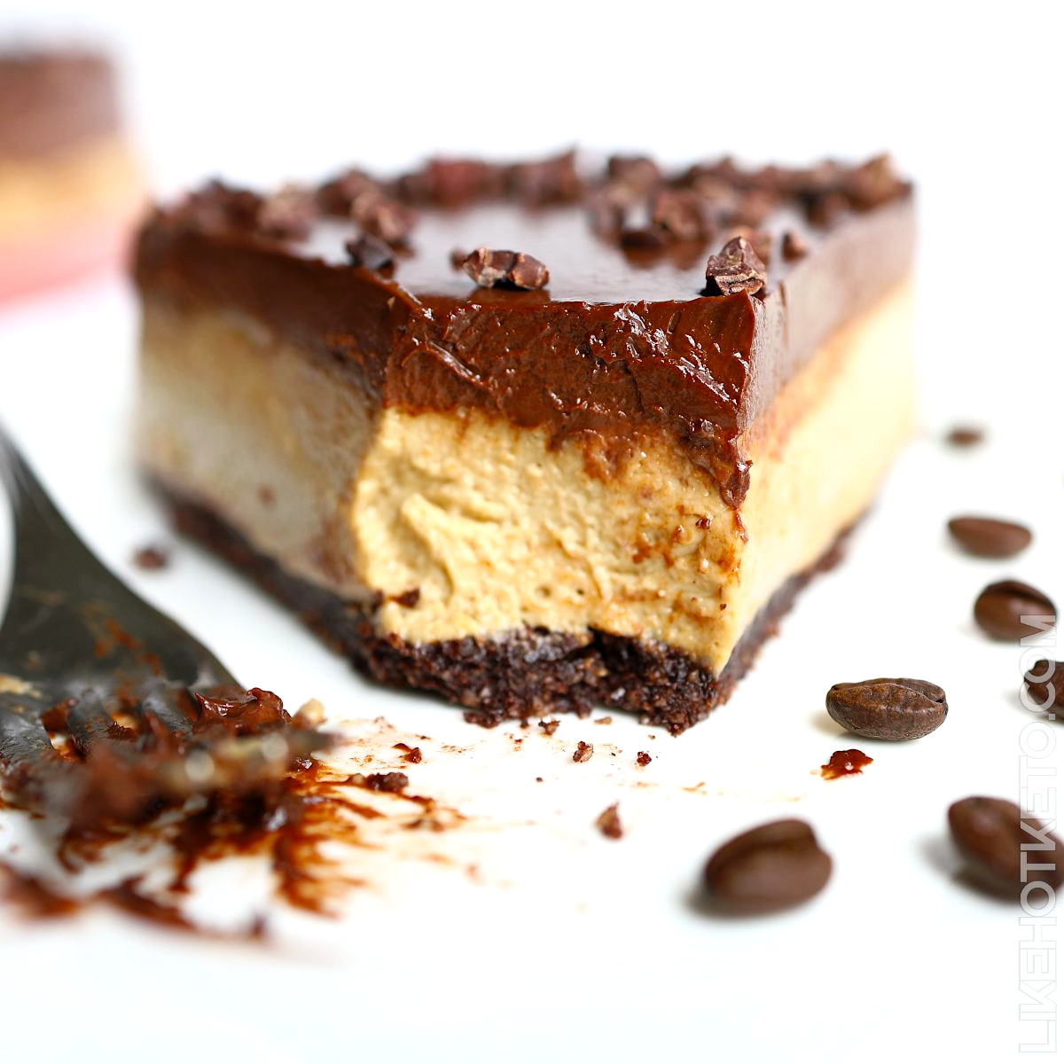 Slice of mocha coffee cheesecake topped with a thick layer of creamy chocolate ganache, with a bite taken of by a fork, resting on the side.