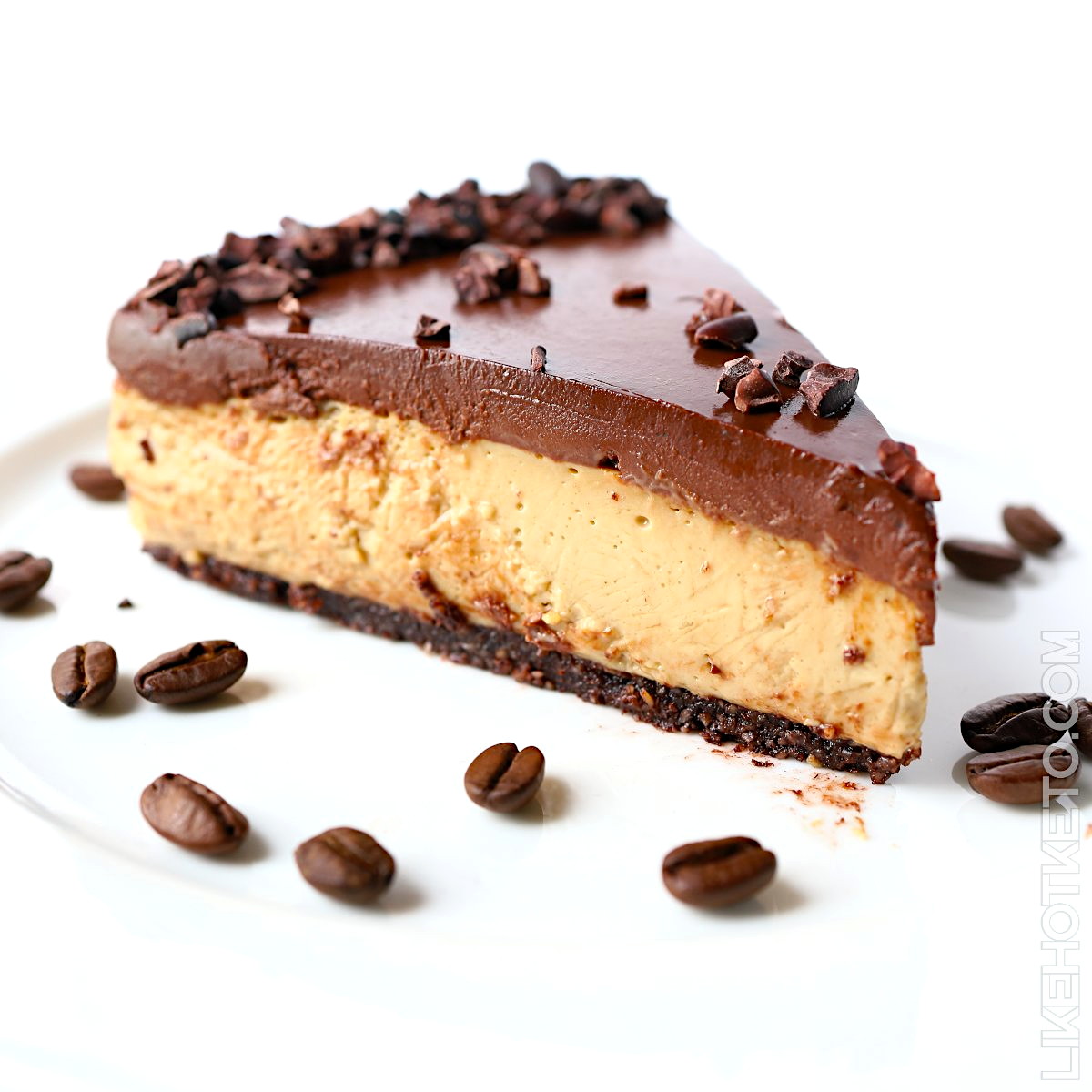 Slice of keto mocha no-bake cheesecake topped with a thick layer of chocolate ganache, decorated with cacao nibs and coffee beans.