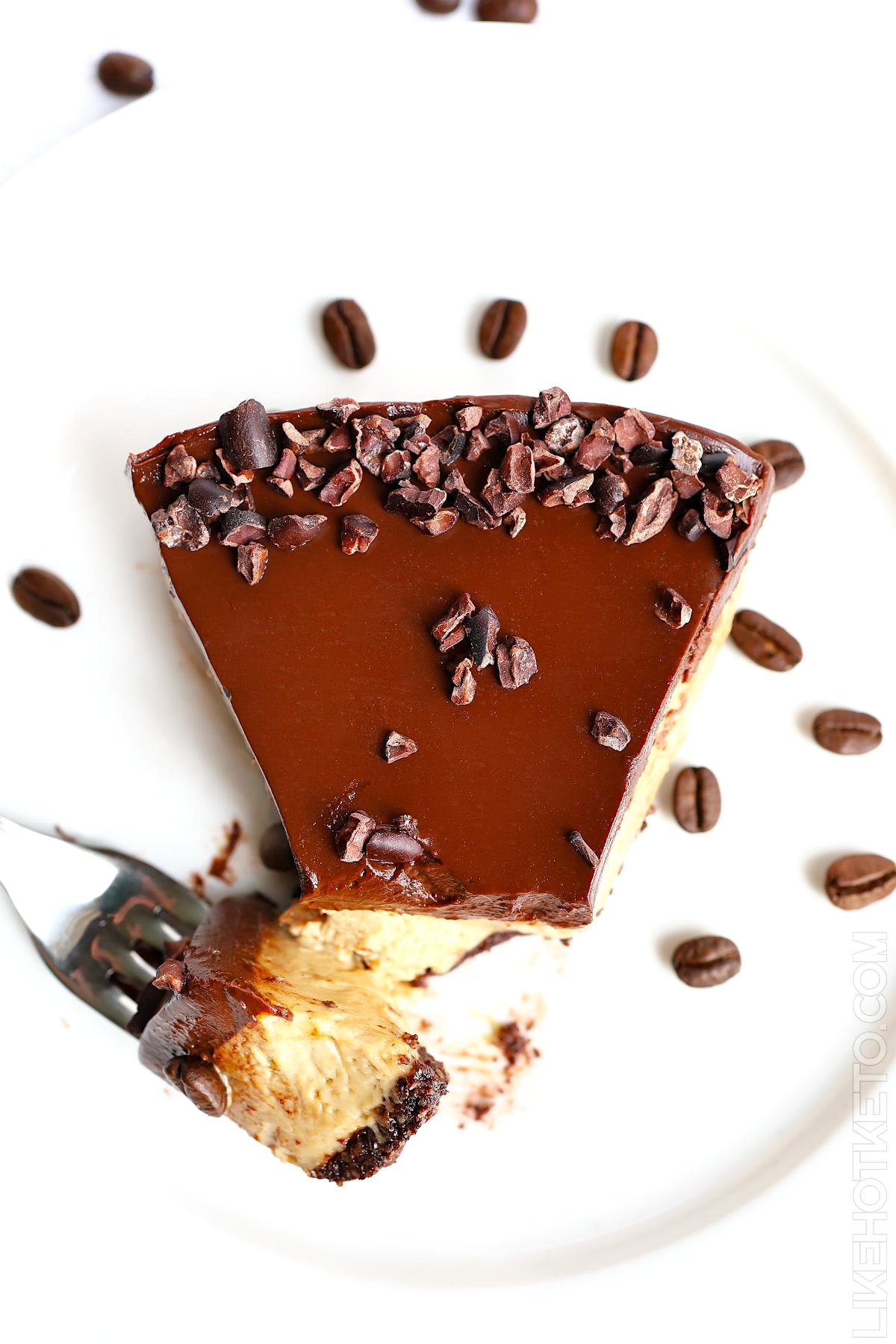 Top view of a slice of keto mocha cheesecake with a creamy ganache topping, with a bite taken of by a fork, resting on the side.