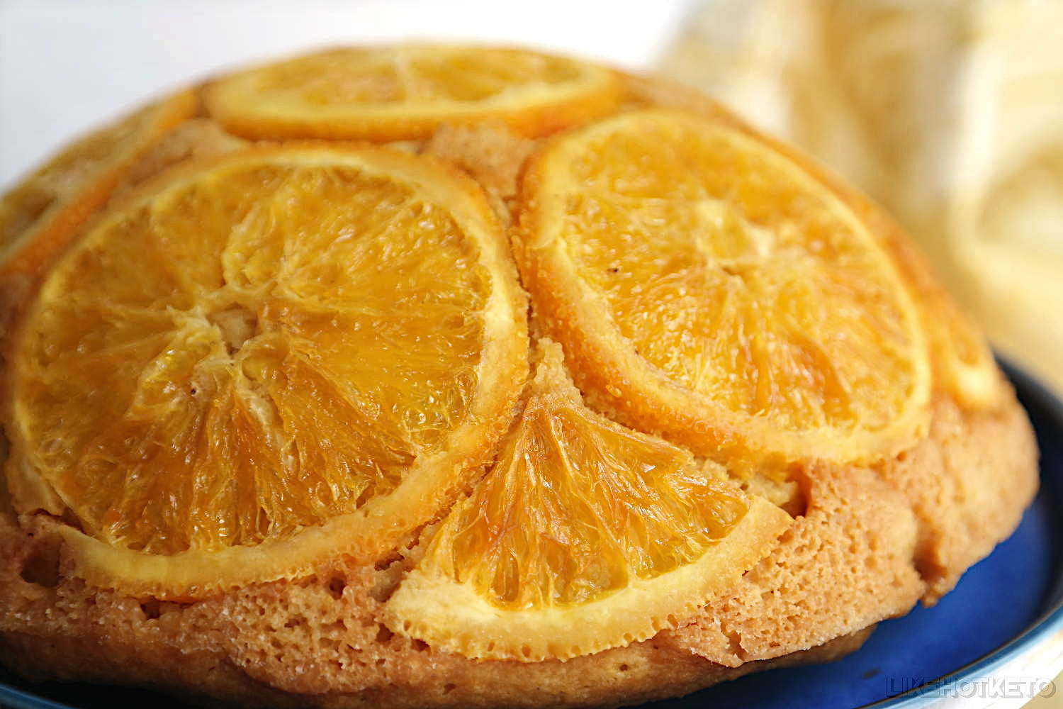 A beautiful smiling fluffy hemisphere shaped cake, covered in golden orange slices.