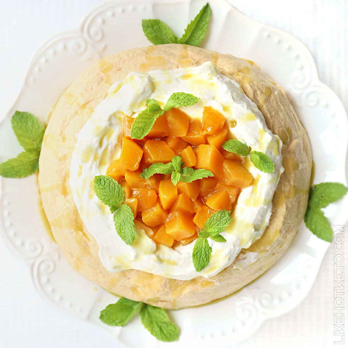 Sugar-free pavlova topped with summer peaches and cream and garnished with mint leaves.