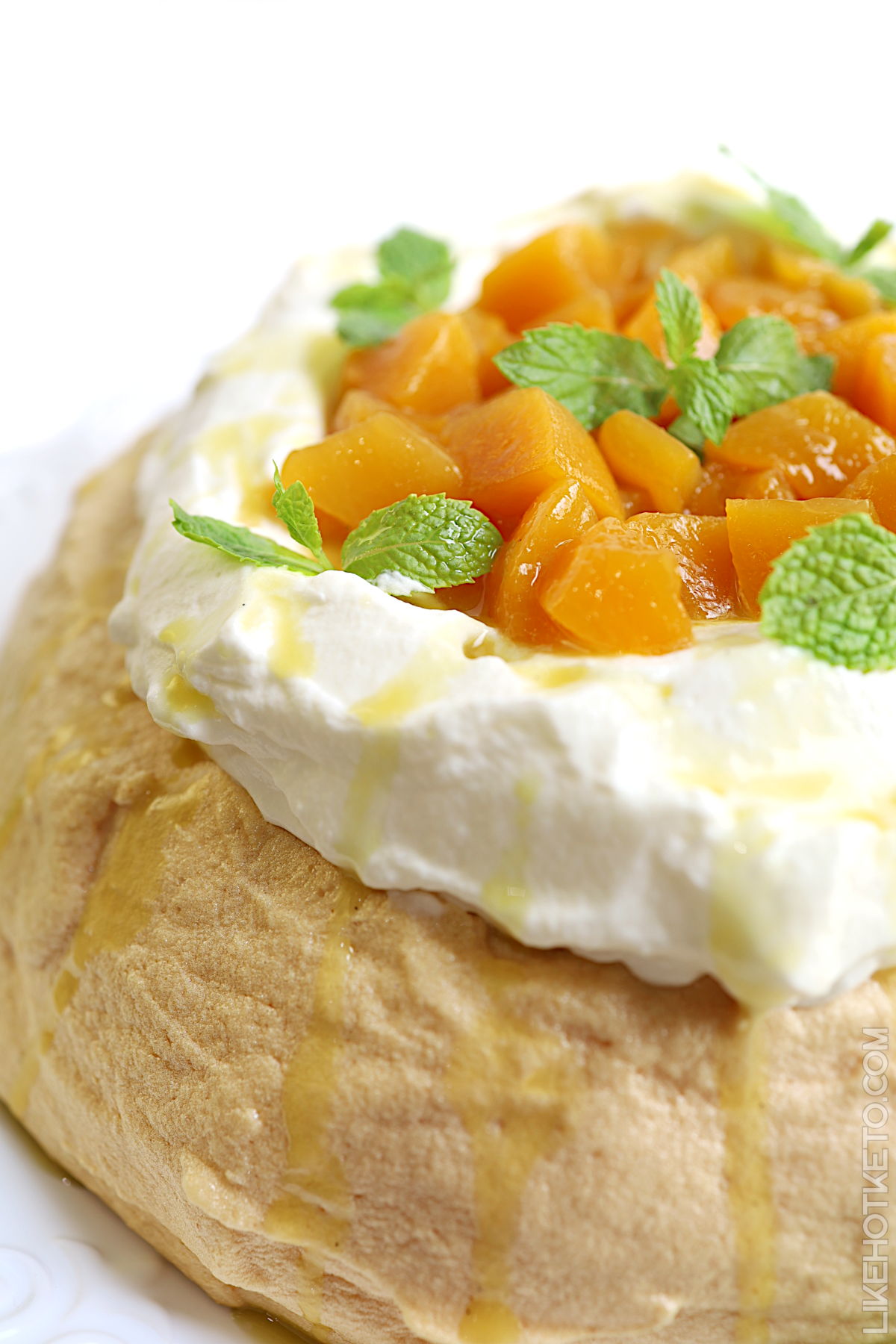 Low-carb pavlova topped with summer peaches and cream and garnished with mint leaves.