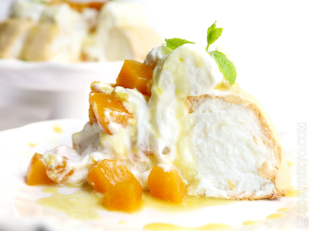 Slice of keto pavlova covered in whipped cream and diced peaches in sugar-free syrup.