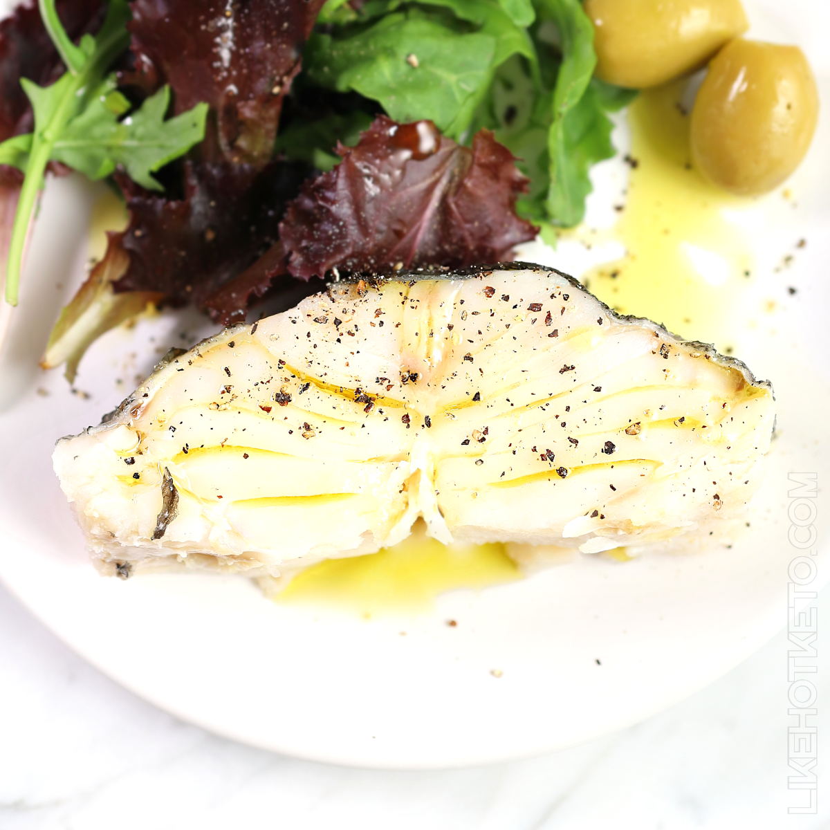Poached cod fillet drizzled with olive oil on a white plate.