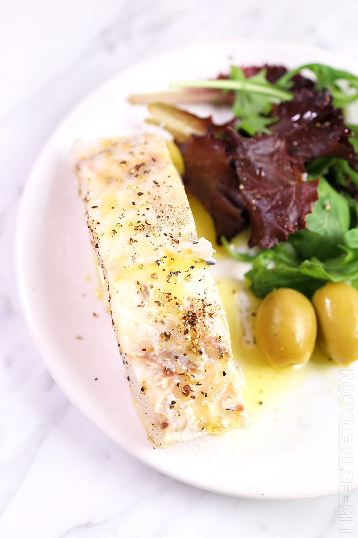 Cooked cod fillet topped with olive oil and cracked peppercorns.