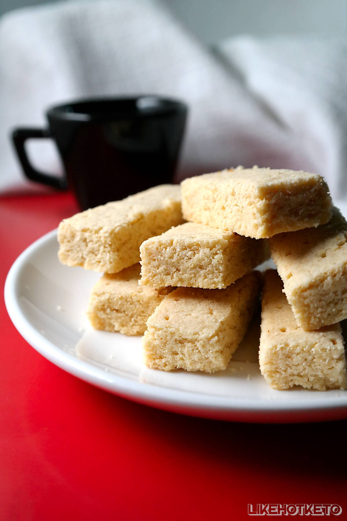 Keto pure butter Scottish shortbread cookies piled up on a small plate, with a tea cup on the side.