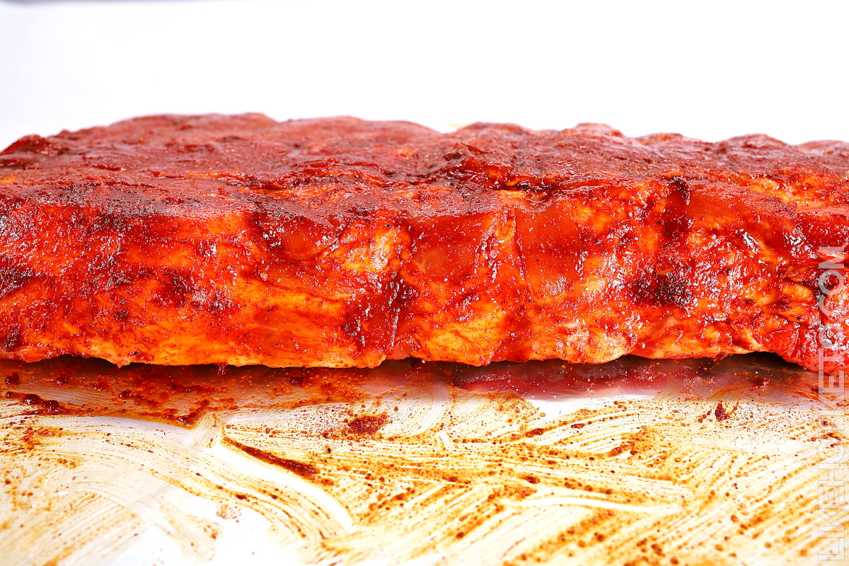 Raw rack of baby ribs rubbed in sugar-free rub, resting on aluminum foil.