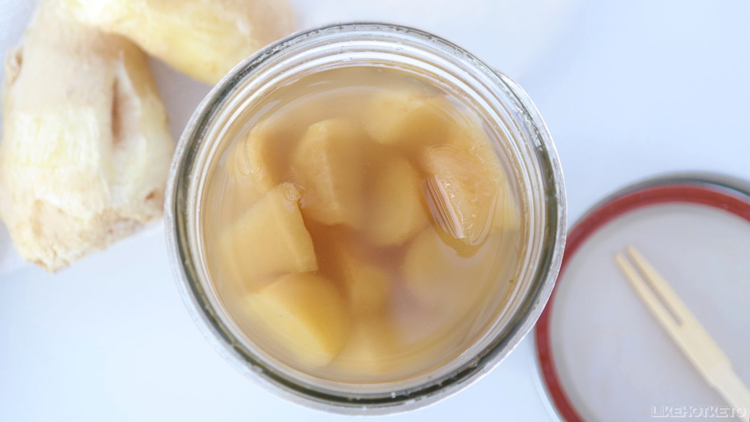 An open glass jar filled with homemade preserved ginger in erythritol syrup.