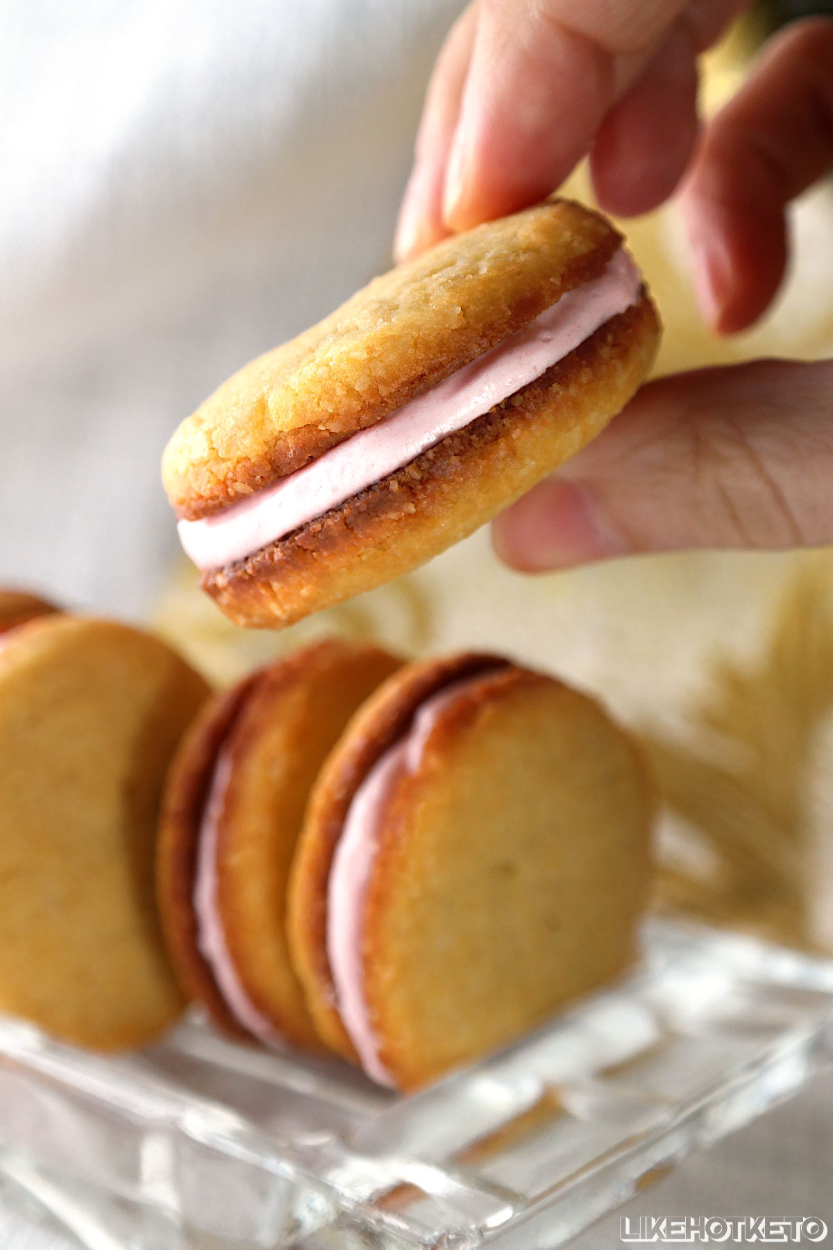 A keto homemade strawberry cream sandwich cookie, held between fingers.