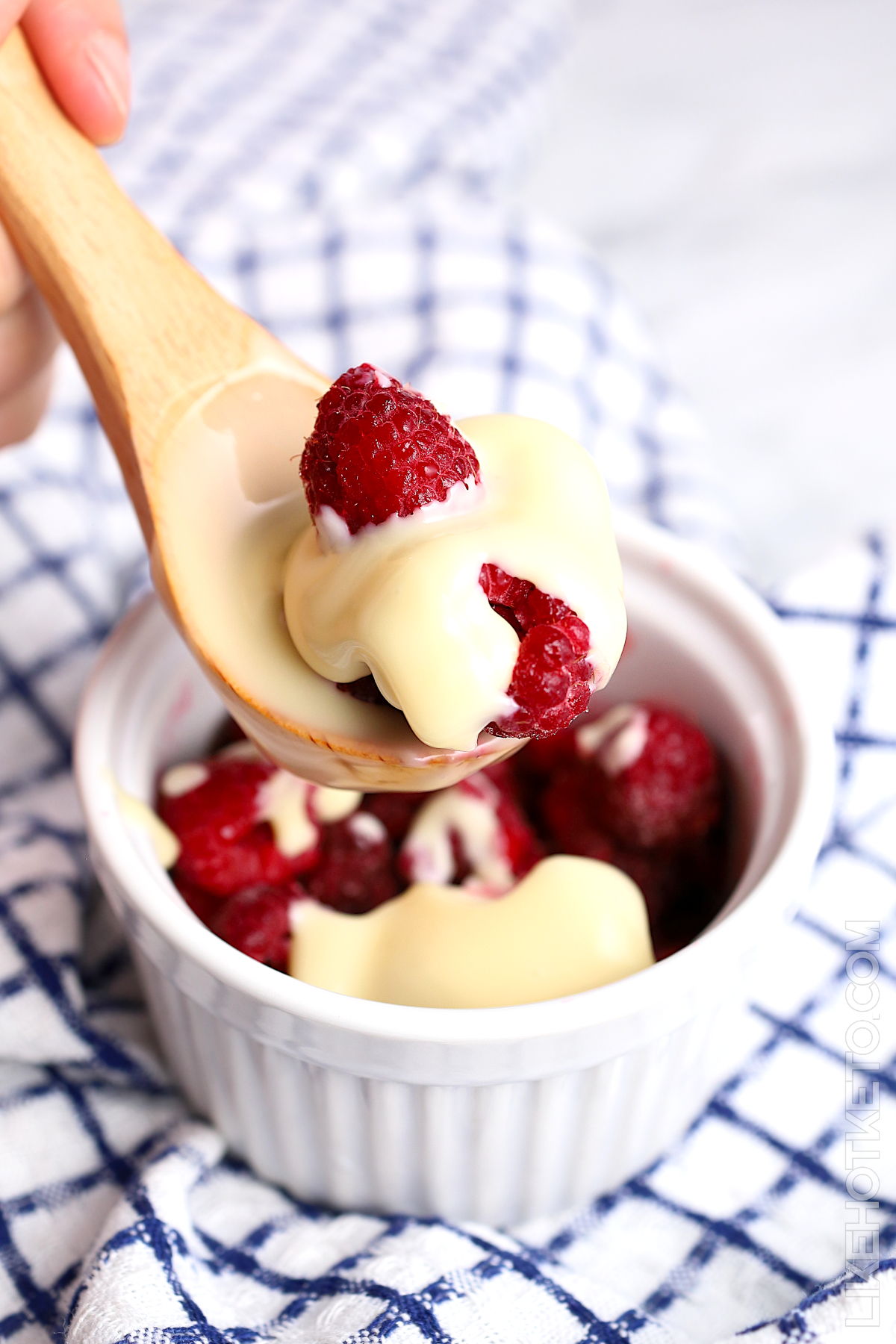 Sugar-free condensed milk over fresh raspberries in a white ramekin and spoon.