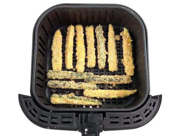 Uncooked zucchini fries neatly arranged in an air fryer basket.