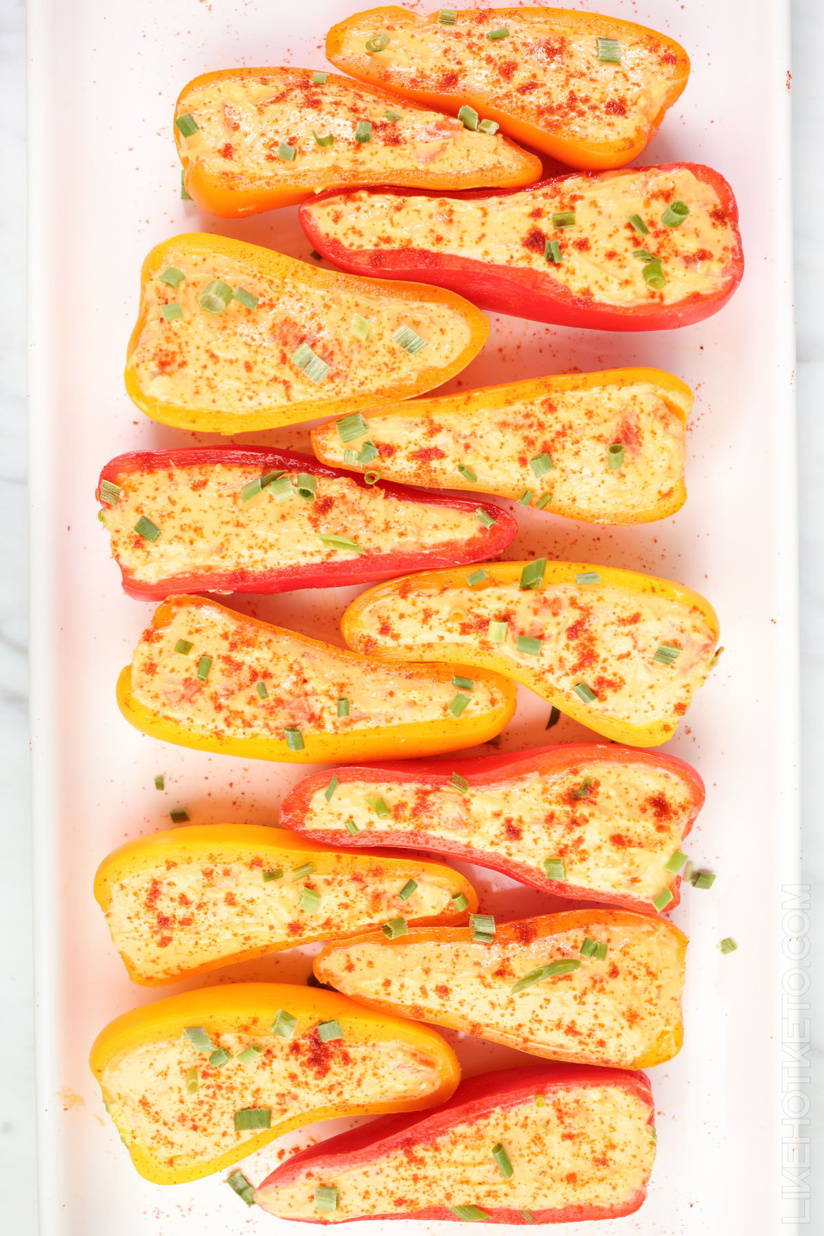 Raw mini bell peppers stuffed with cream cheese mix, garnished with spring onions.