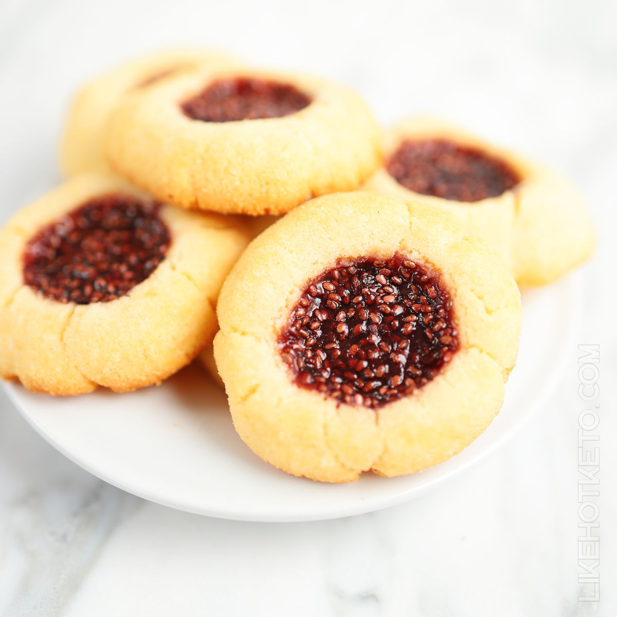 Sugar-free jam thumbprint cookies piled up on a white plate.