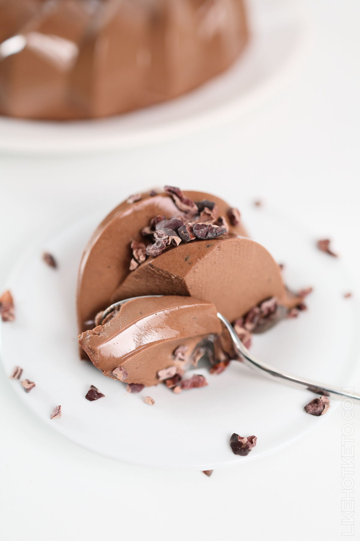 Chocolate jello getting sliced by spoon on a white plate.