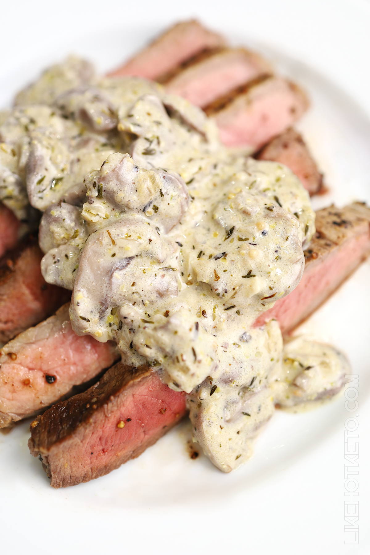Creamy keto mushroom butter & garlic sauce topping thick slices of medium-rare pink steak, on a white plate.