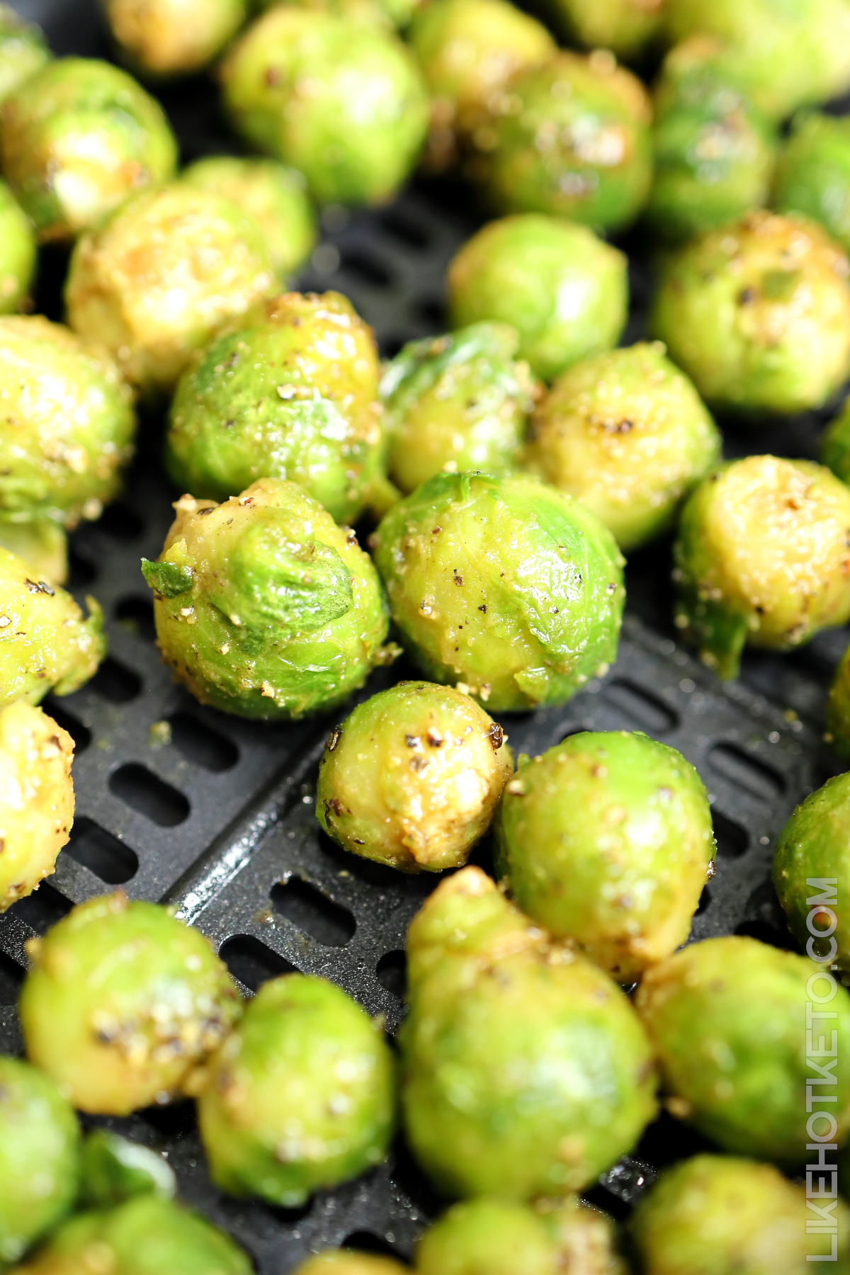 Frozen Brussel sprouts coated in oil and spices, inside an air fryer basket.