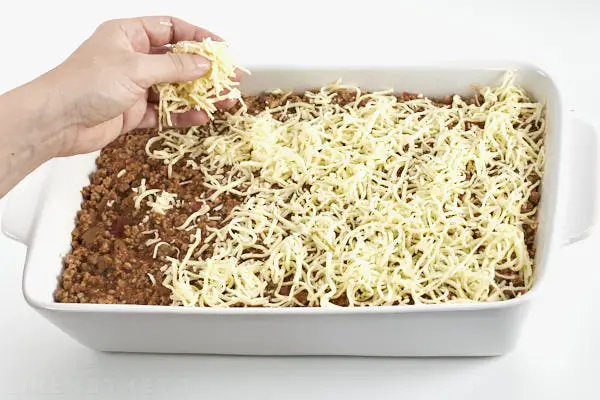 Sprinkling shredded cheese over the meat sauce layer.