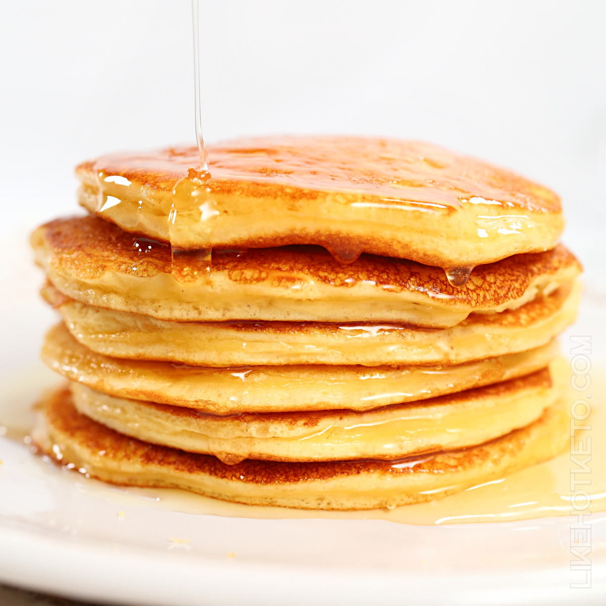A stack of fluffy protein pancakes being poured with keto maple syrup.