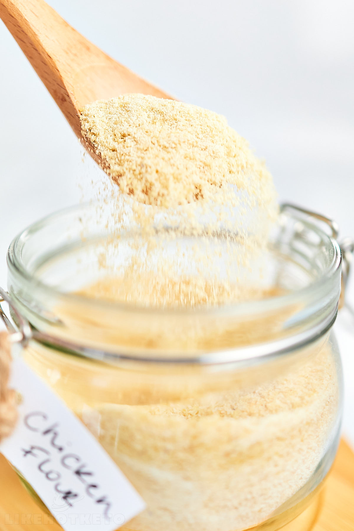 Fine granules of dehydrated chicken powder falling from a spoon into a jar.