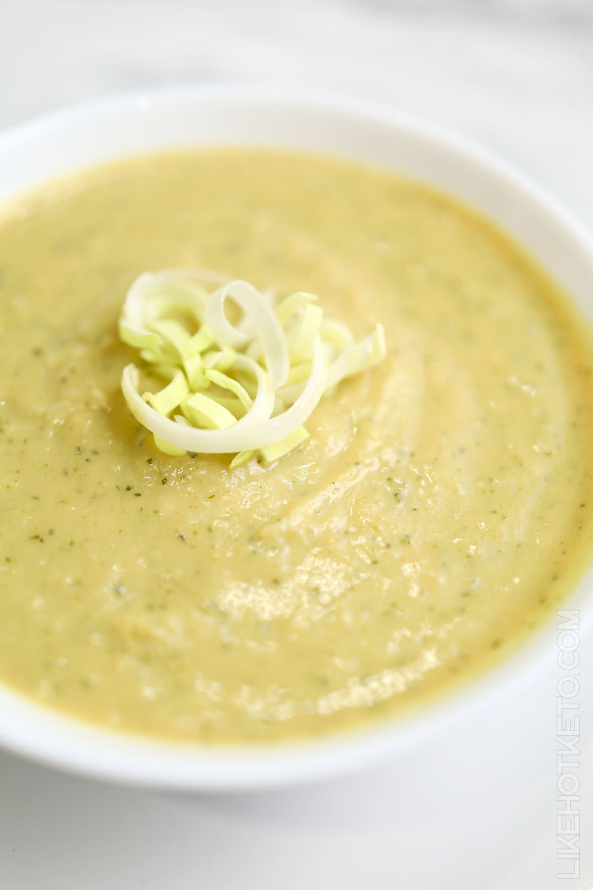 Bowl of zucchini and pea protein soup garnished with leeks.
