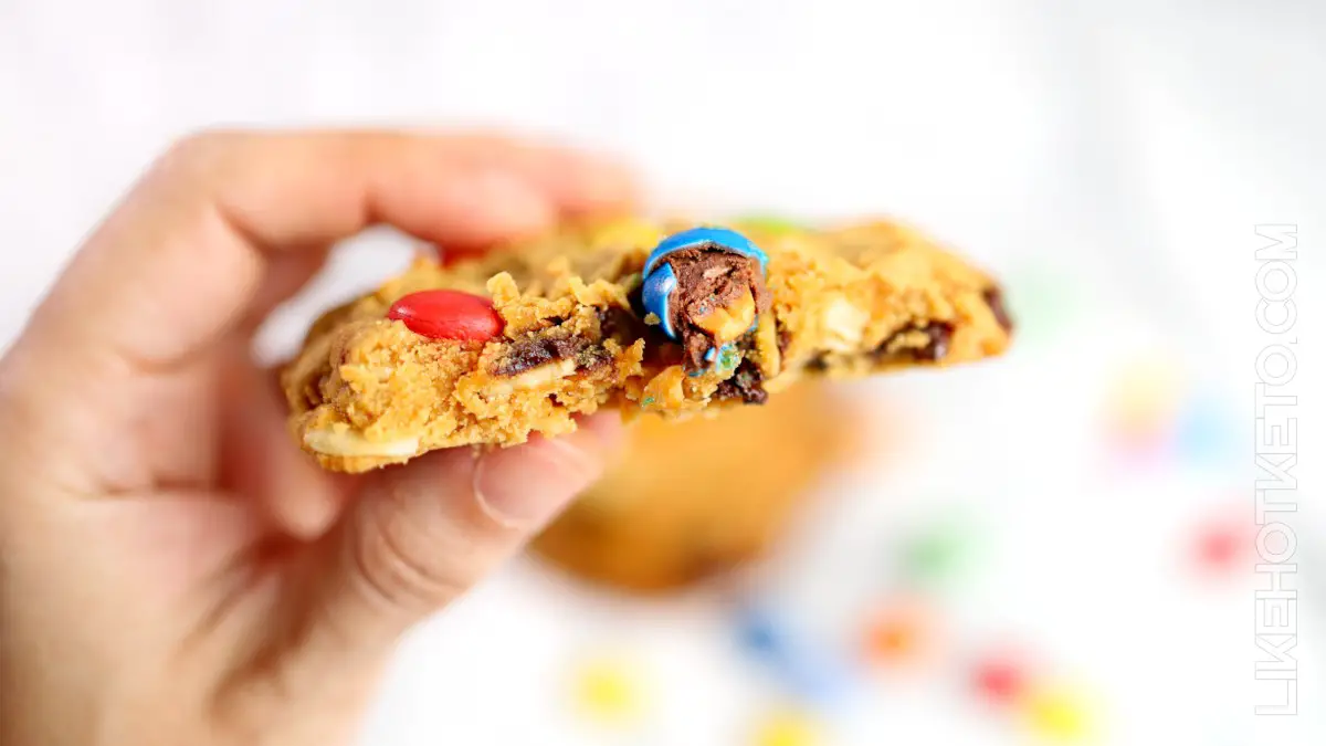 A half bitten keto monster cookie with soft interior and melted M&M's pieces.