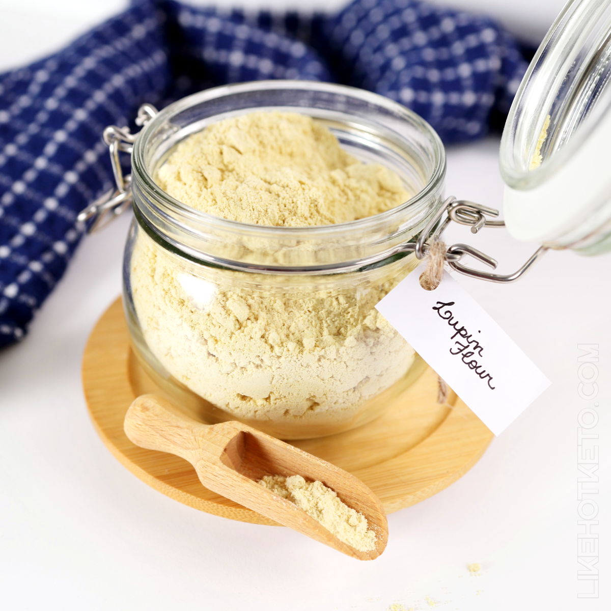 Open mason jar filled with lupin flour, and lupin flour on a wooden spoon.