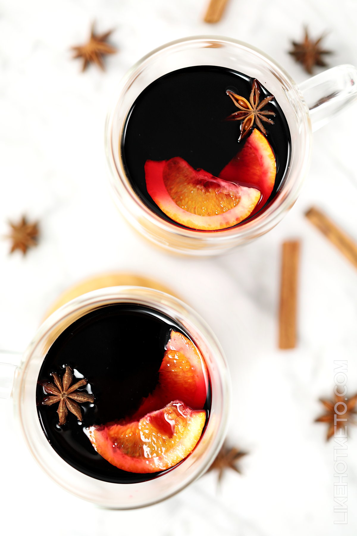 Two cups of keto mulled wine, with cinnamon sticks, star anise, and orange slices.