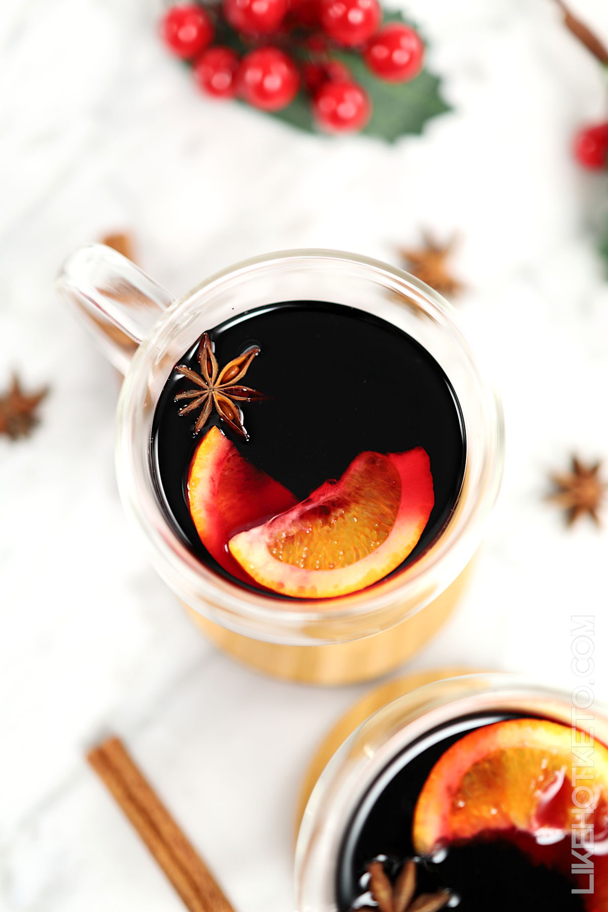 Cups of mulled wine with oranges, cinnamon and star anise and Christmas decorations on the background.