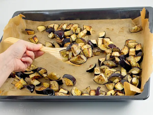 Golden roasted eggplants with charred edges on baking tray.
