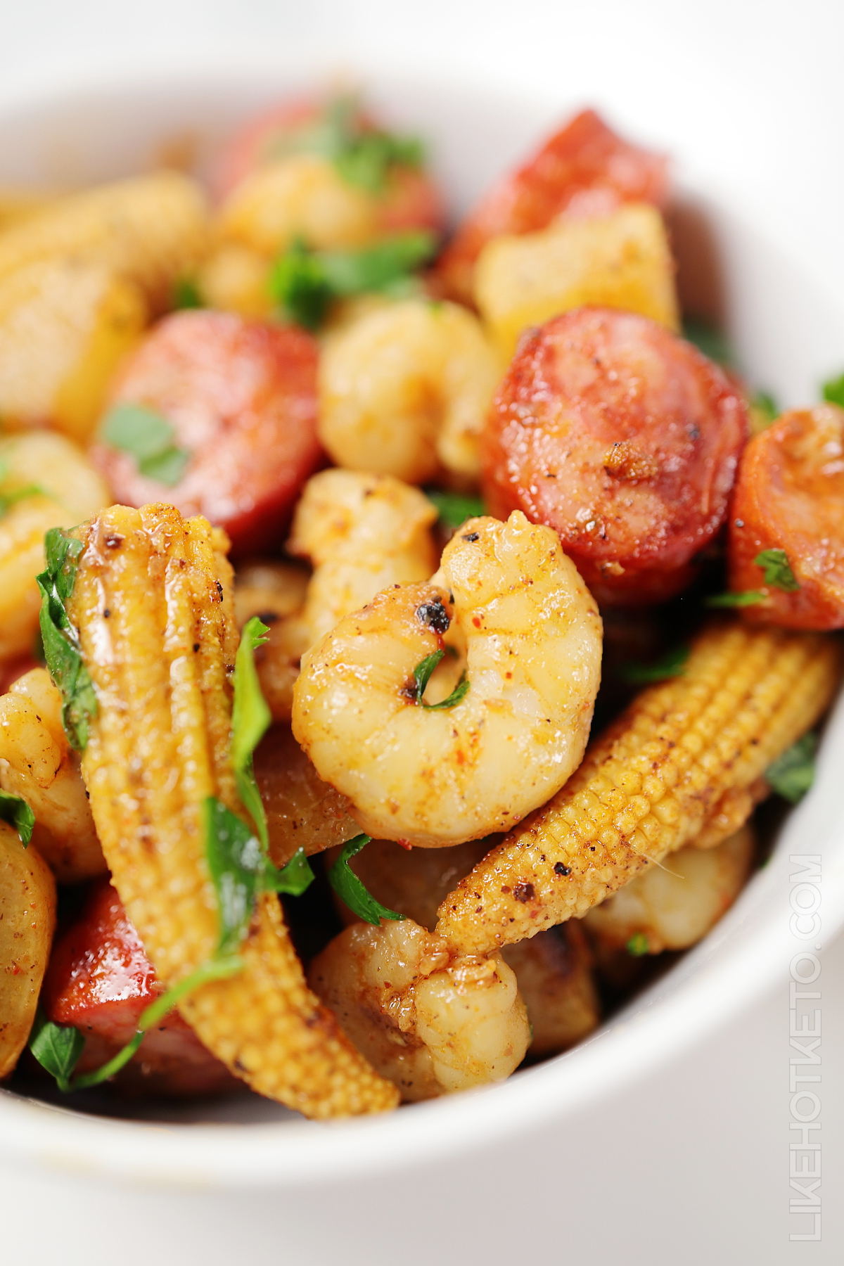 Low-carb seafood boil with shrimp and andouille sausages in a white bowl.