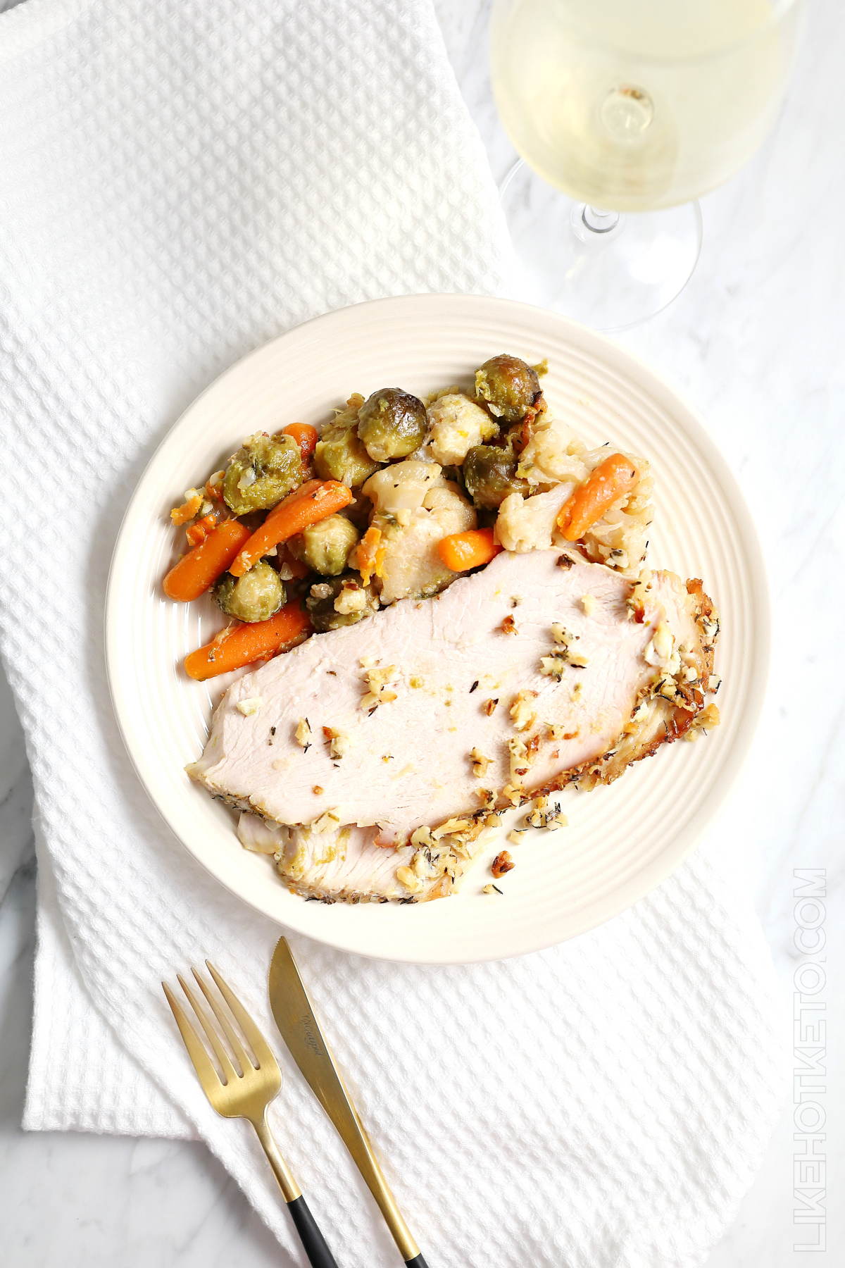 A generous serving of sliced skinless turkey breast and roasted keto veggies, with a glass of white wine.