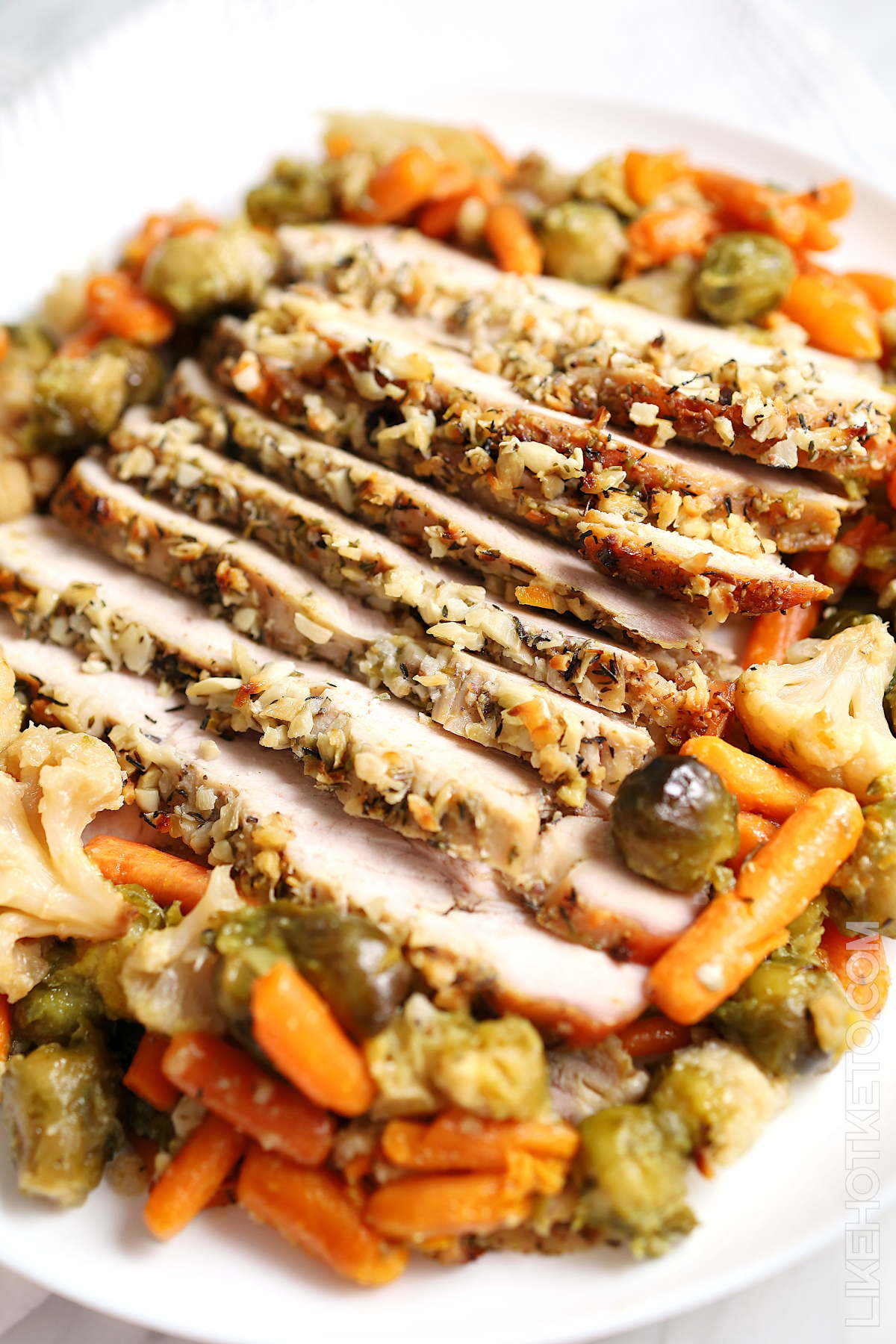 A large serving plate with roasted garlic butter turkey breast surrounded with baby carrots, Brussel sprouts and cauliflower.