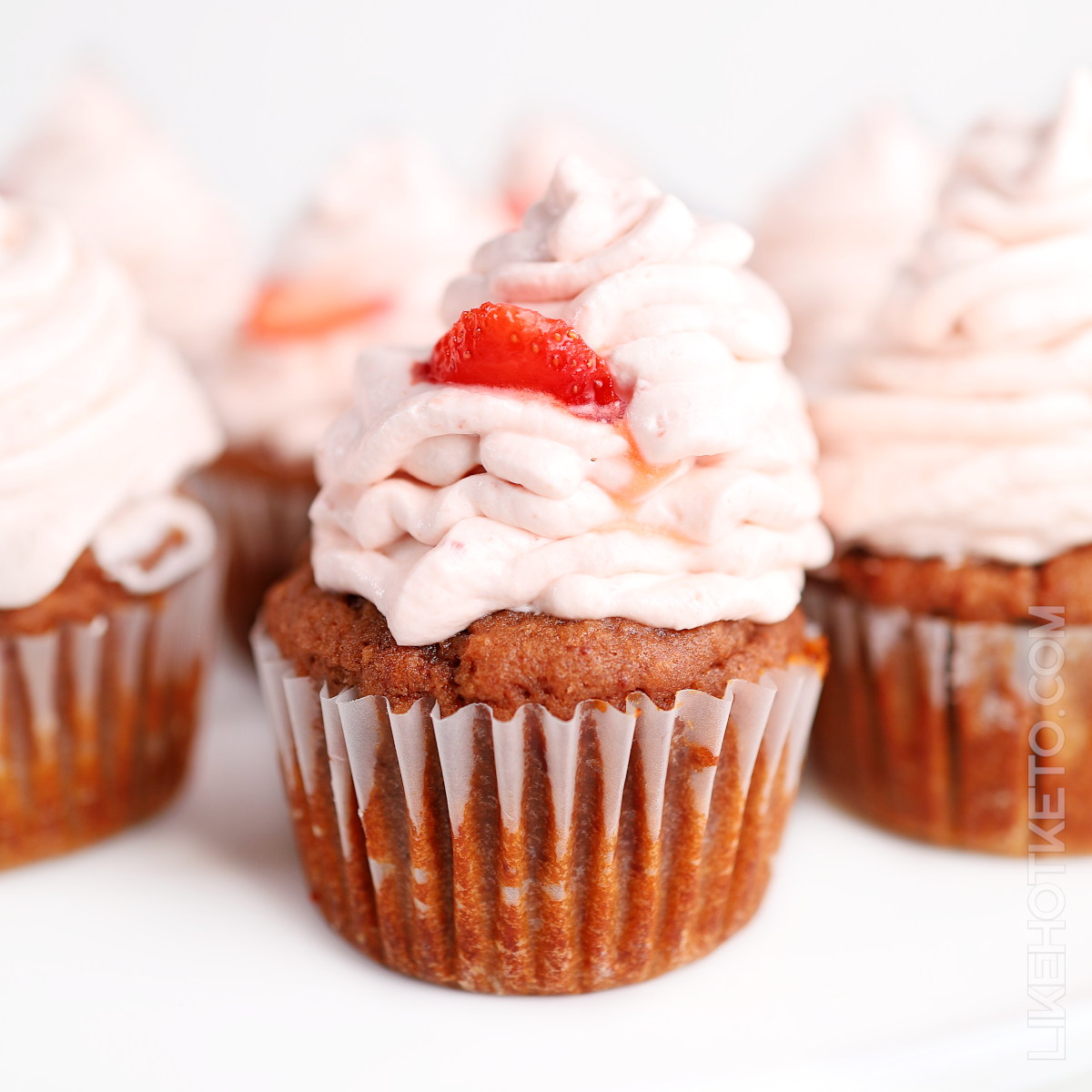 Pink keto strawberry cupcake with a tall strawberry cream cheese frosting and a strawberry slice.