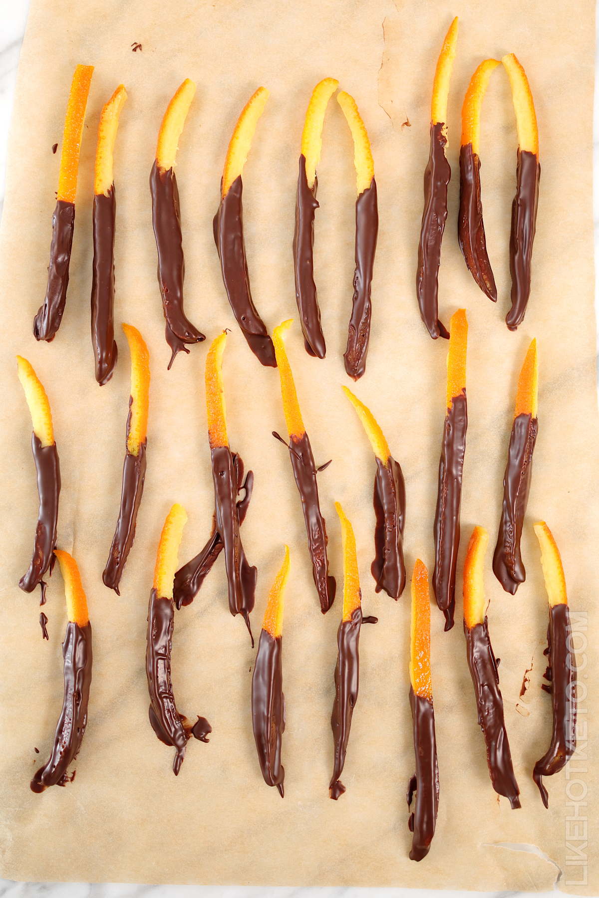 Keto candied orange peels freshly dipped in melted chocolate spread on a parchment paper to set.