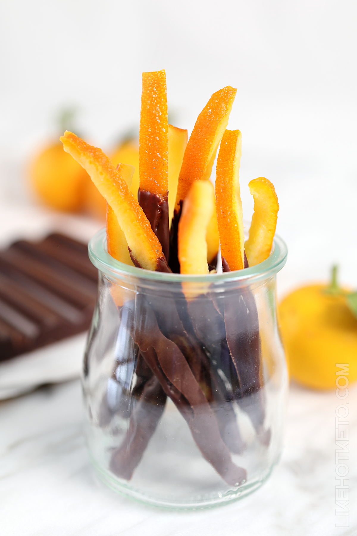 Keto candied orange peels dipped in dark chocolate in a small glass.