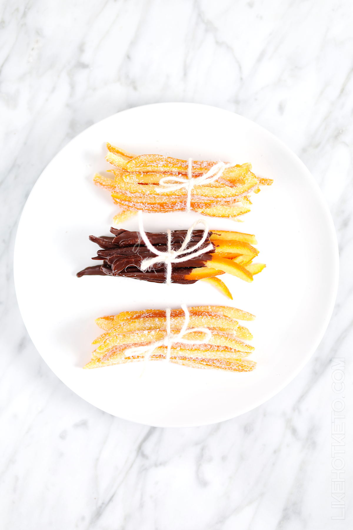 Bundles of sugar-free candied orange peels, dipped in chocolate ad in granulated sweetener, tied up with strings on a plate.